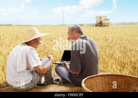 Two farmers sitting in field talking Stock Photo