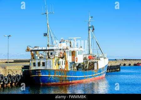 Simrishamn, Sweden - April 1, 2016: A rusty blue and white fishing boat moored in the harbor. Car tires hang at the pier as bump Stock Photo