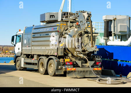 Simrishamn, Sweden - April 1, 2016: A MAN TGS flush truck parked beside a blue and white fishing boat in the harbor. Pipes lead Stock Photo