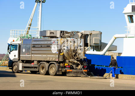 Simrishamn, Sweden - April 1, 2016: A MAN TGS flush truck parked beside a blue and white fishing boat in the harbor. Pipes lead Stock Photo