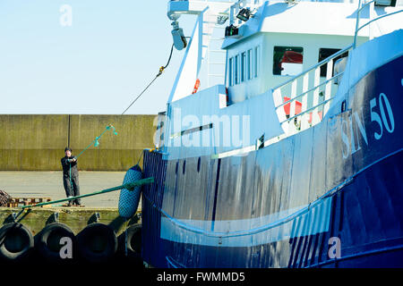 Simrishamn, Sweden - April 1, 2016: One person on dockside pull on a rope from a fishing boat. A thin rope is used to get a thic Stock Photo