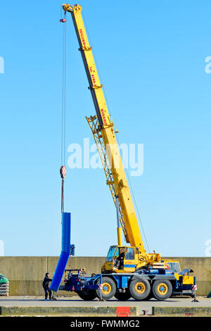 Simrishamn, Sweden - April 1, 2016: Yellow Liebherr mobile crane lifting a blue trawler wing off the ground at port. Normal work Stock Photo
