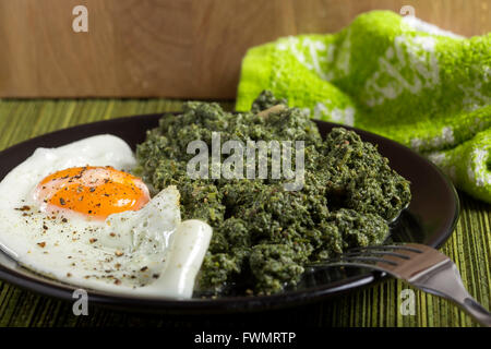 Stewed nettles with garlic and one egg on dark plate with fork Stock Photo