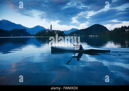 Man canoeing on Lake Bled, Slovenia with the island church of the assumption of saint mary, the clifftop castle in the backgroun Stock Photo