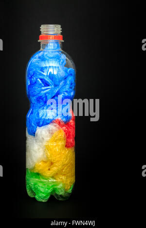 Plastic water bottle full of plastic shopping bags on black background. Concept image for polluting water and oceans Stock Photo