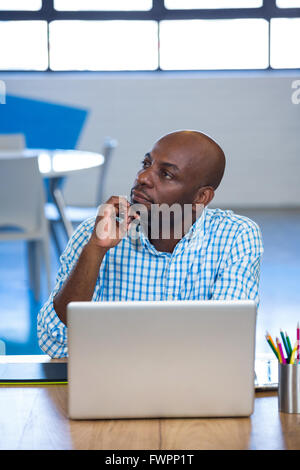 Thoughtful man sitting on table with laptop Stock Photo