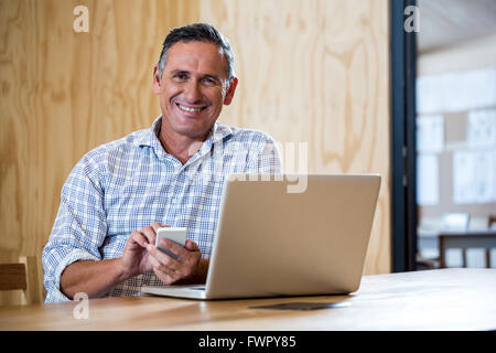 Smiling senior man using smartphone and laptop Stock Photo