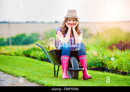 Woman sitting in wheelbarrow in sunny green garden Stock Photo