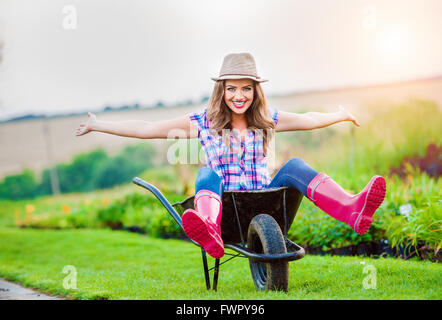 Woman sitting in wheelbarrow in sunny green garden Stock Photo