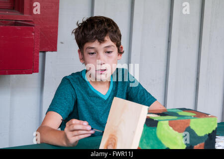 boy at camp painting a birdhouse craft project Stock Photo