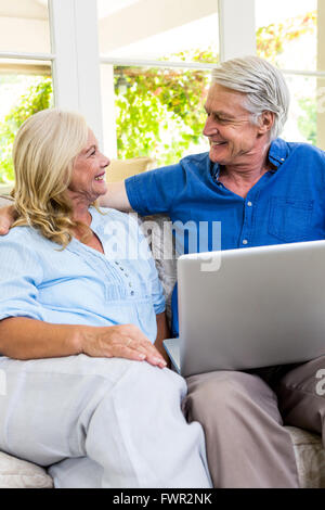 Happy senior couple with laptop while sitting on sofa at home Stock Photo
