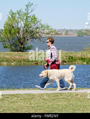 A middle-aged Caucasian woman walks her Labrador Retriever on the Overholser lake trails inh Oklahoma City, Oklahoma,USA. Stock Photo