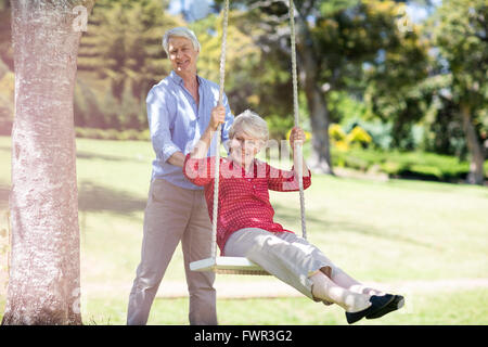 Senior man pushing his partner on swing Stock Photo