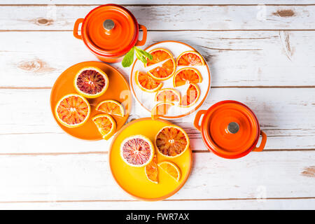 Blood oranges sliced on plates with orange cast iron pots on white wood Stock Photo