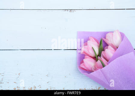 Beautiful bouquet of pink tulips in violet paper on light wooden background Stock Photo