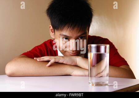 Kid looking at a glass of water on a wooden table Stock Photo