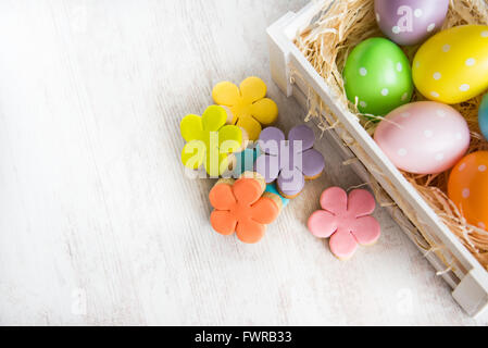 Wooden basket filled with easter eggs and homemade fondant covered flower cut cookies on a white wooden background Stock Photo