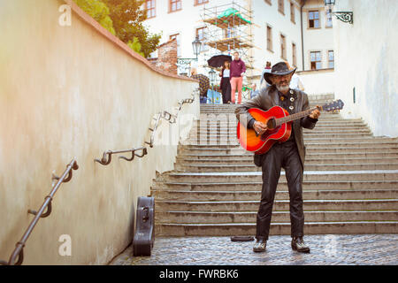 PRAGUE, CZECH REPUBLIC - AUGUST 25, 2015: Street musician with a hat and with a guitar on the stairs high in the District Mala Stock Photo