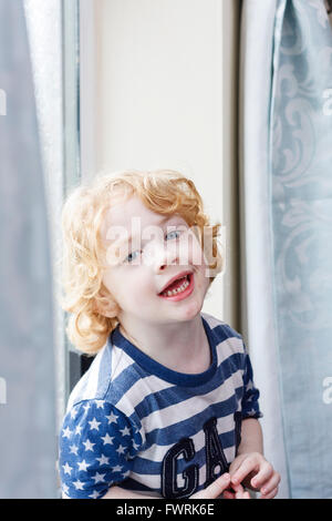 A small caucasion blond haired boy sat by a window, smiling Stock Photo