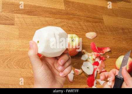 A hand holding a peeled apple over a pile of peelings Stock Photo