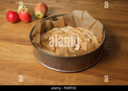 Unbaked apple pie in a metal spring form with fresh apples lying next to it, on a wood table Stock Photo