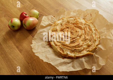Freshly baked apple pie on baking paper with apples lying next to it Stock Photo