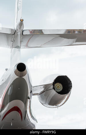A private jet on a tarmac behind a wire fence on a dark, cloudy day in