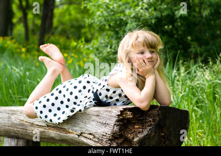 beautiful blond girl lying on wooden bench in forrest Stock Photo