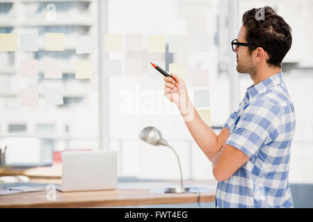 Thoughtful man reading at sticky notes on window Stock Photo