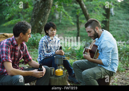 Multi-ethnic group of friends playing guitar at a camp site Stock Photo