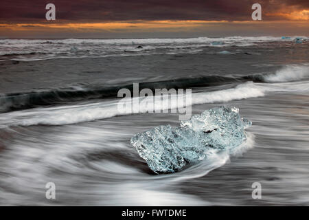 Melting block of ice washed on beach along the Atlantic Ocean coastline at Breidamerkursandur black sands in winter, Iceland