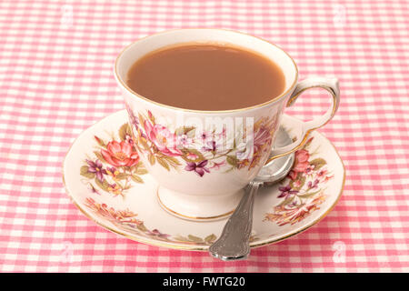 A hot cup of tea served in an antique patterned tea cup and saucer, all placed on a checked pattern tablecloth. Stock Photo