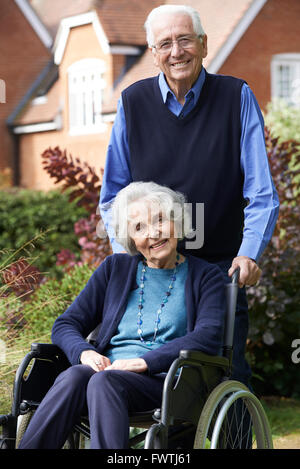 Senior Woman In Wheelchair Being Pushed By Husband Stock Photo