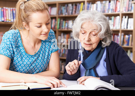Senior Woman Working With Teacher In Library Stock Photo