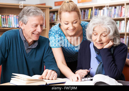 Mature Students Working With Teacher In Library Stock Photo