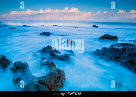 Waves washing up on beach rocks at sunrise in Napili Bay with Molokai in background, Maui Stock Photo