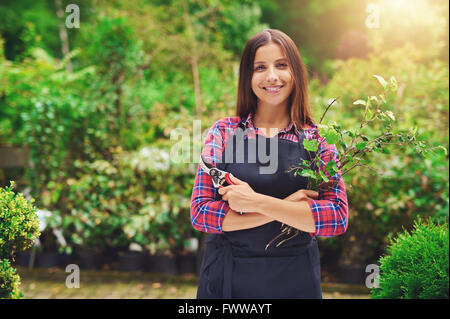 Happy confident attractive young woman pruning plants in a nursery as she celebrates her success as an entrepreneur with her own Stock Photo