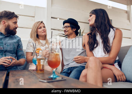 Group of young people sitting around a table chatting. Young friends together partying, with cocktails on table. Stock Photo