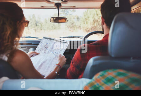 Rear view shot of couple driving on country road. Woman holding a route map with man driving the car. Couple on adventurous road Stock Photo