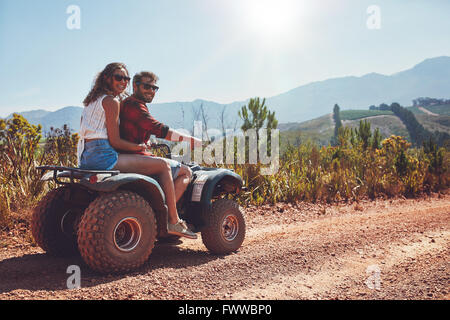 Portrait of loving couple in nature on a off road vehicle. Young man and woman enjoying a quad bike ride in countryside. Stock Photo