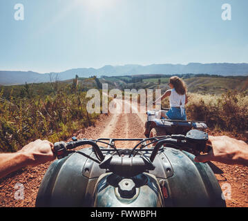 Young people on quad bikes on a countryside trail. View from a quad bike with woman driving an ATV in front on a sunny day. Stock Photo