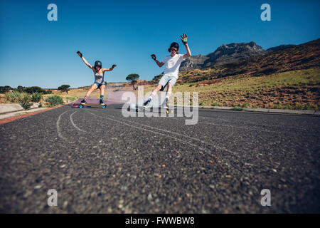Young people skateboarding with smoke bomb on the road. Young man and woman practicing skating on a rural road. Stock Photo