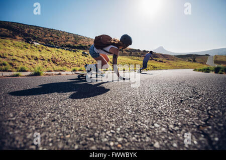 Young friends skating with their skateboards on rural road. Young people longboarding down the road on sunny day. Stock Photo
