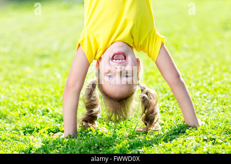 kid girl standing upside down on her head on grass in summer Stock Photo