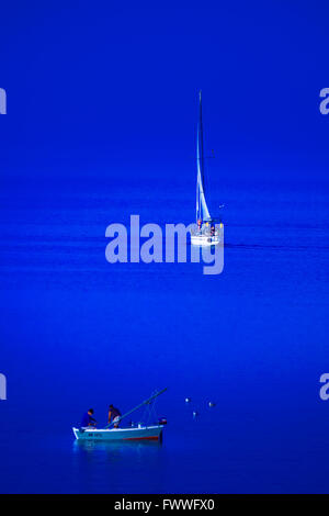 Small fishing boat and sailing boat meet in the blue sea. Stock Photo