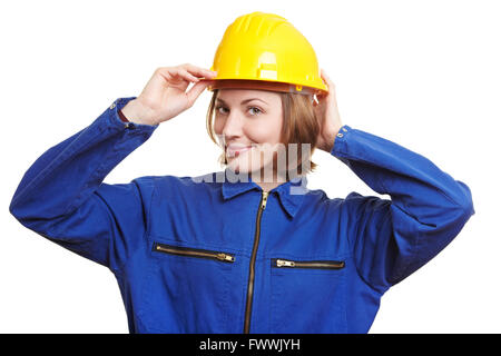 Smiling woman with blue overall putting on safety helmet Stock Photo