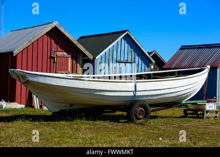 Simrishamn, Sweden - April 1, 2016: White traditional hunting canoe on a trailer in front of red and blue fishing cabins. Stock Photo