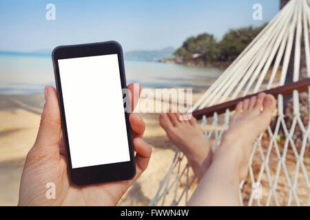 mobile application for travels, hand holding smart phone with white screen on the beach Stock Photo