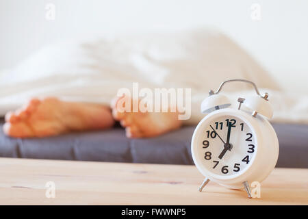 alarm clock and feet of sleeping person, morning concept, wake up Stock Photo