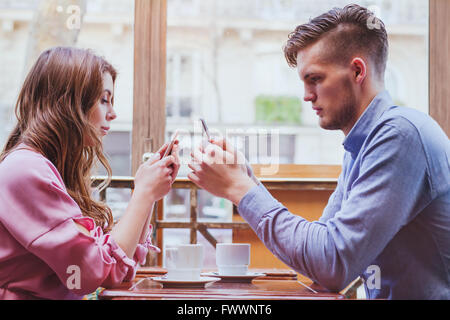 always connected, internet addiction, young couple in cafe looking at their smartphones, social network concept Stock Photo